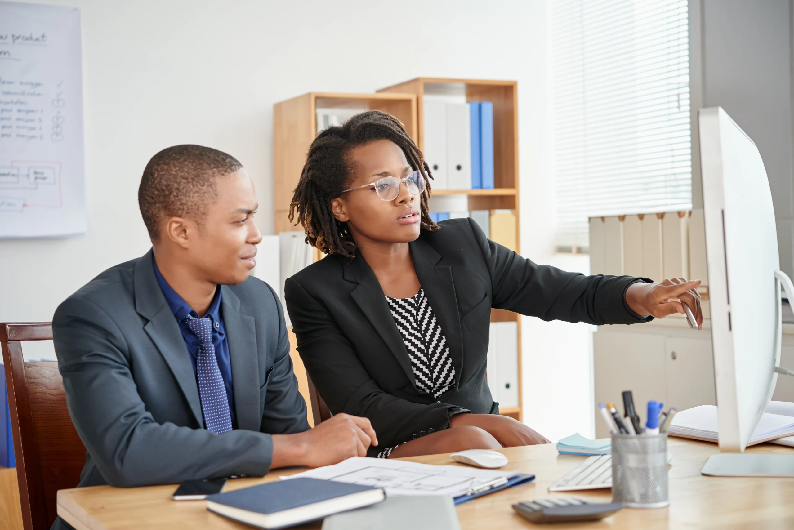 black-male-female-colleagues-sitting-office-looking-computer-screen-together